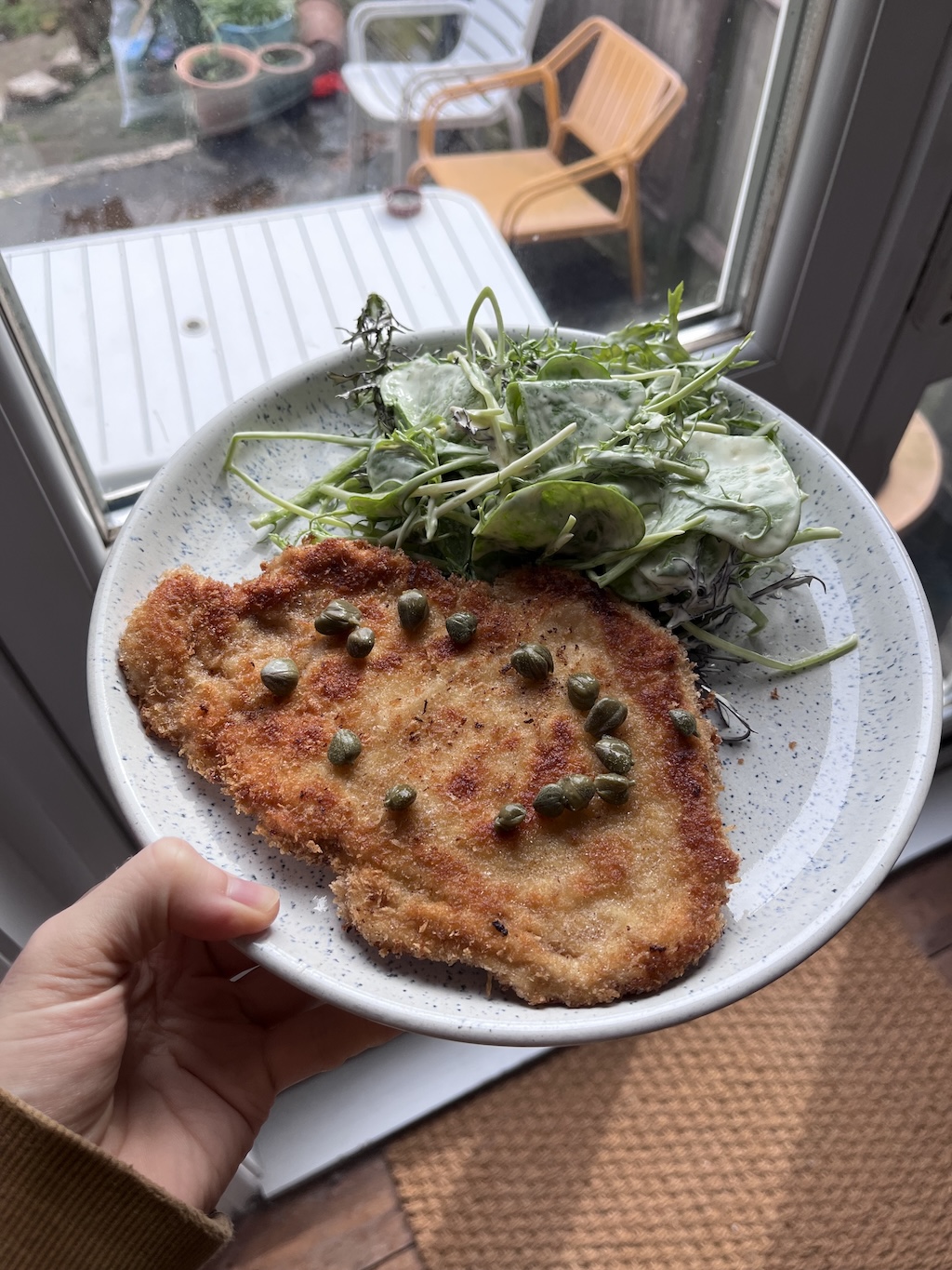 A chicken schnitzel on a plate with a spring salad in a lemon & dijon dressing.